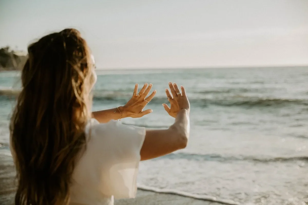 Woman framing the ocean with her hands on a beach at golden hour, for The Ocean Healing Institute