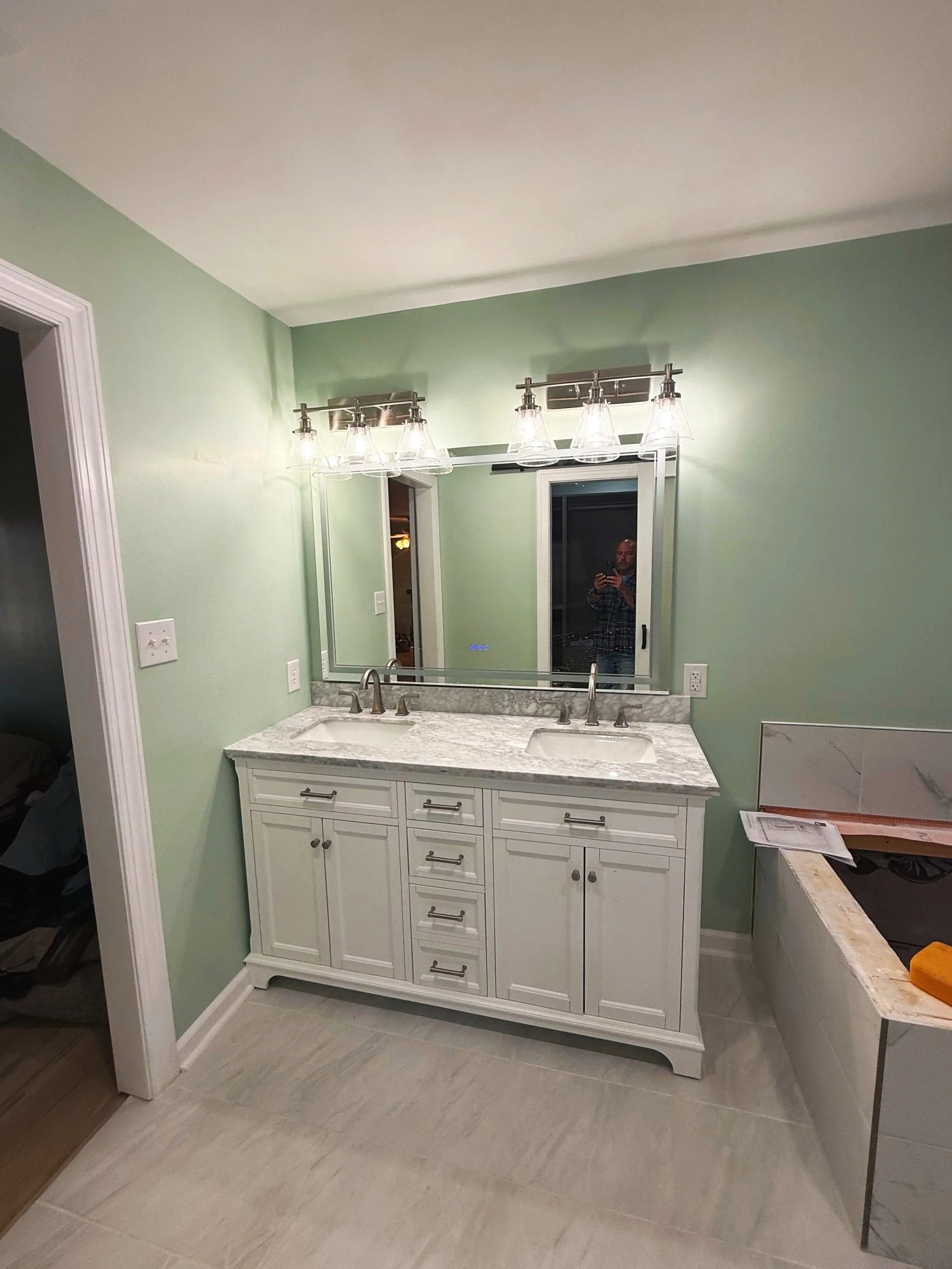 Bathroom vanity with two sinks, white cabinet, marble countertop, large mirror, and modern light fixture with five glass shades.