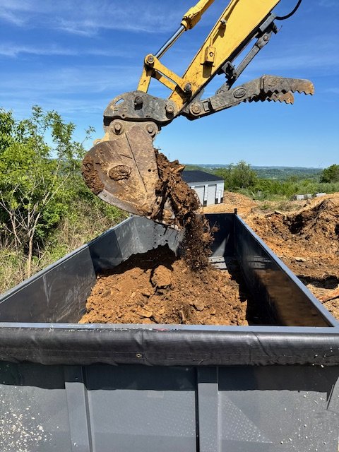 Excavator bucket dumping dirt into a black container outdoors.