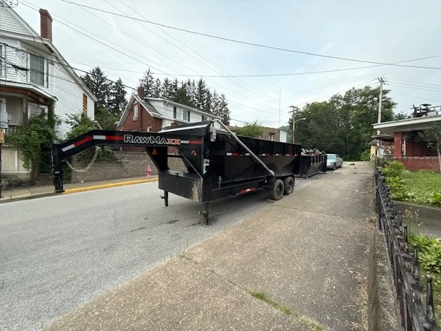 A large black trailer parked on a suburban street, with houses and trees in the background.