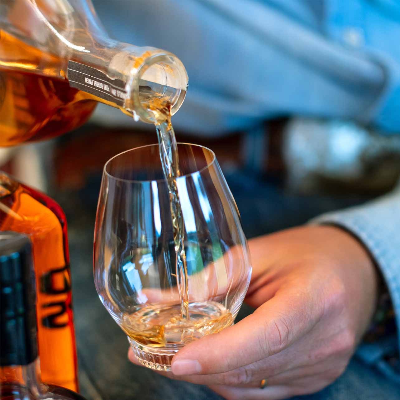 Person pouring whiskey from a bottle into a snifter glass.