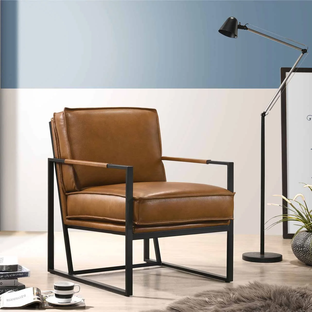 A modern living room with a brown leather armchair, black metal frame, and wooden armrests. Next to it is a black floor lamp with an adjustable arm and black shade. The background wall is painted in a two-tone pattern, light blue above and white below. On the floor are books, a cup, and a fluffy rug.
