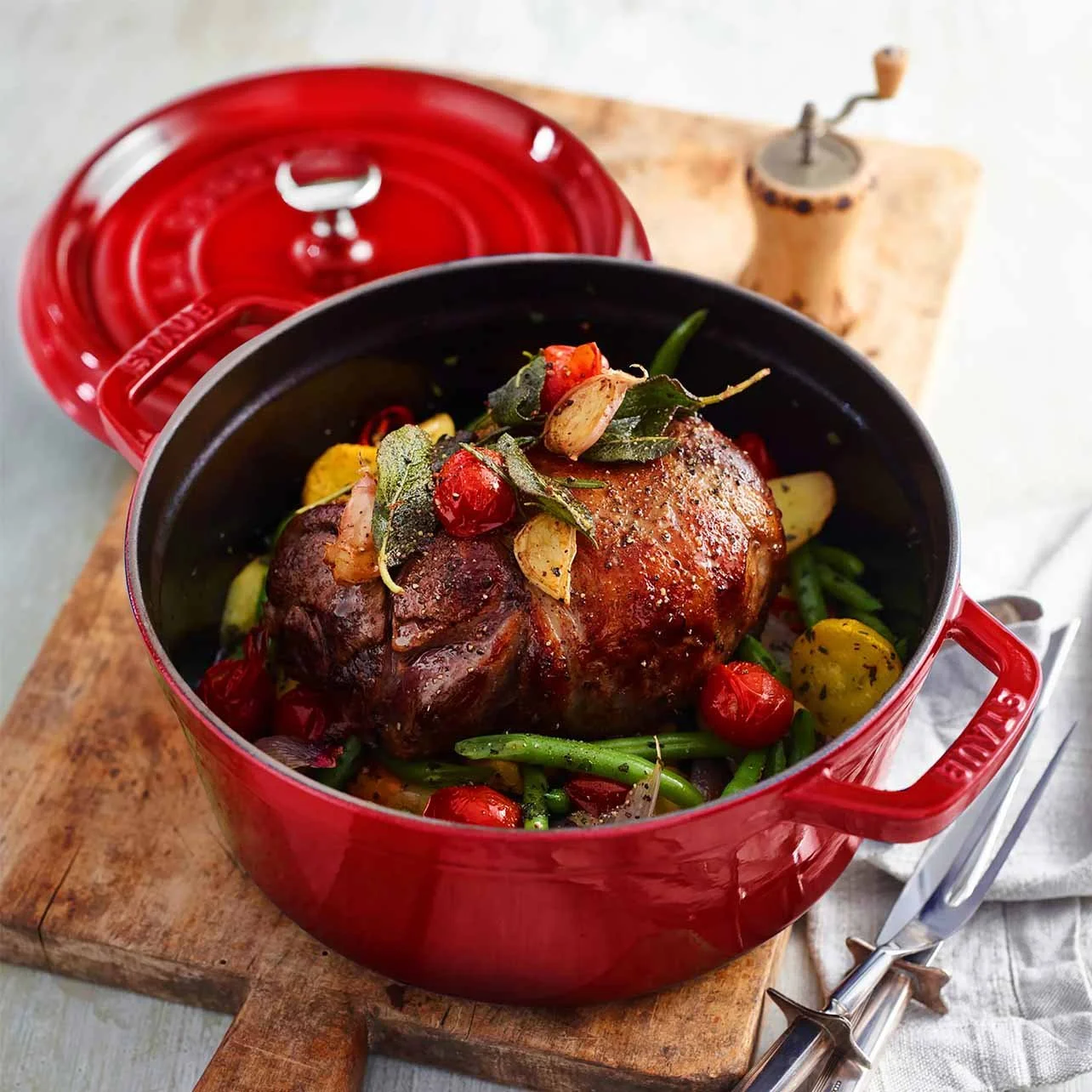 Roasted chicken with vegetables, cherry tomatoes, and herbs in a red cast-iron pot.