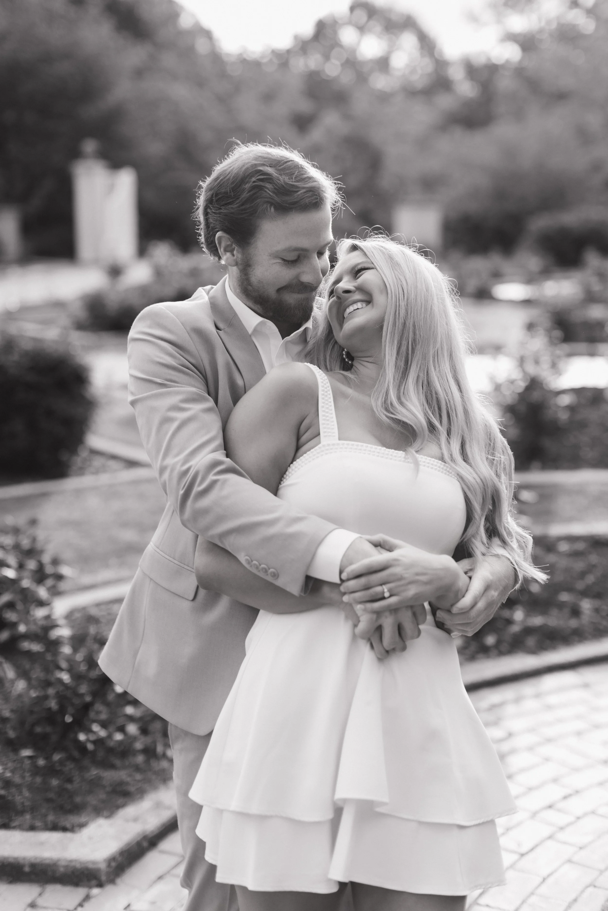 A happy couple embracing outdoors, smiling at each other in a park setting, black and white photo