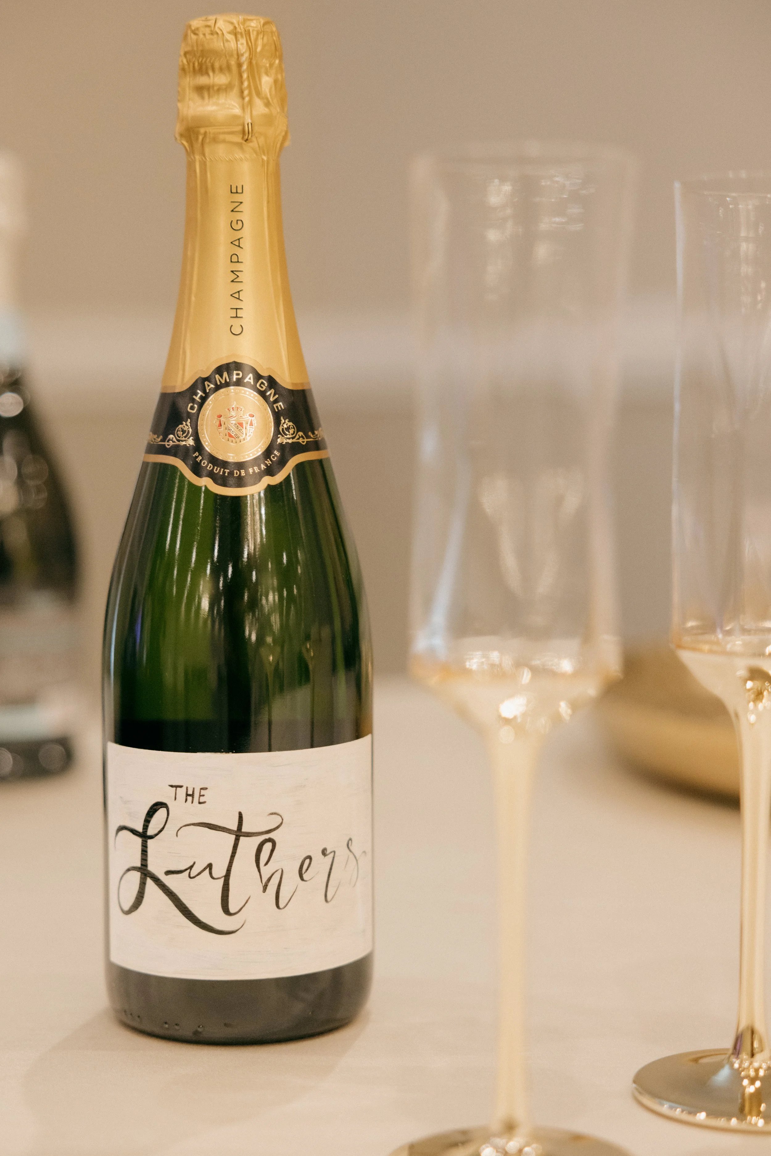 A bottle of champagne labeled 'The Luthers' placed on a table next to two empty champagne flutes.