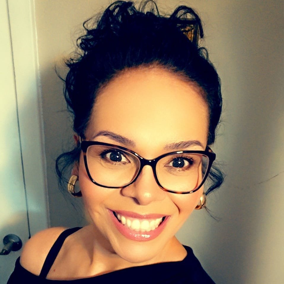 A woman with glasses and earrings, smiling widely, with her dark hair styled in an updo.