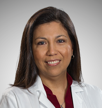 A professional woman with straight dark hair smiling, wearing a white lab coat and a burgundy shirt against a light gray background.
