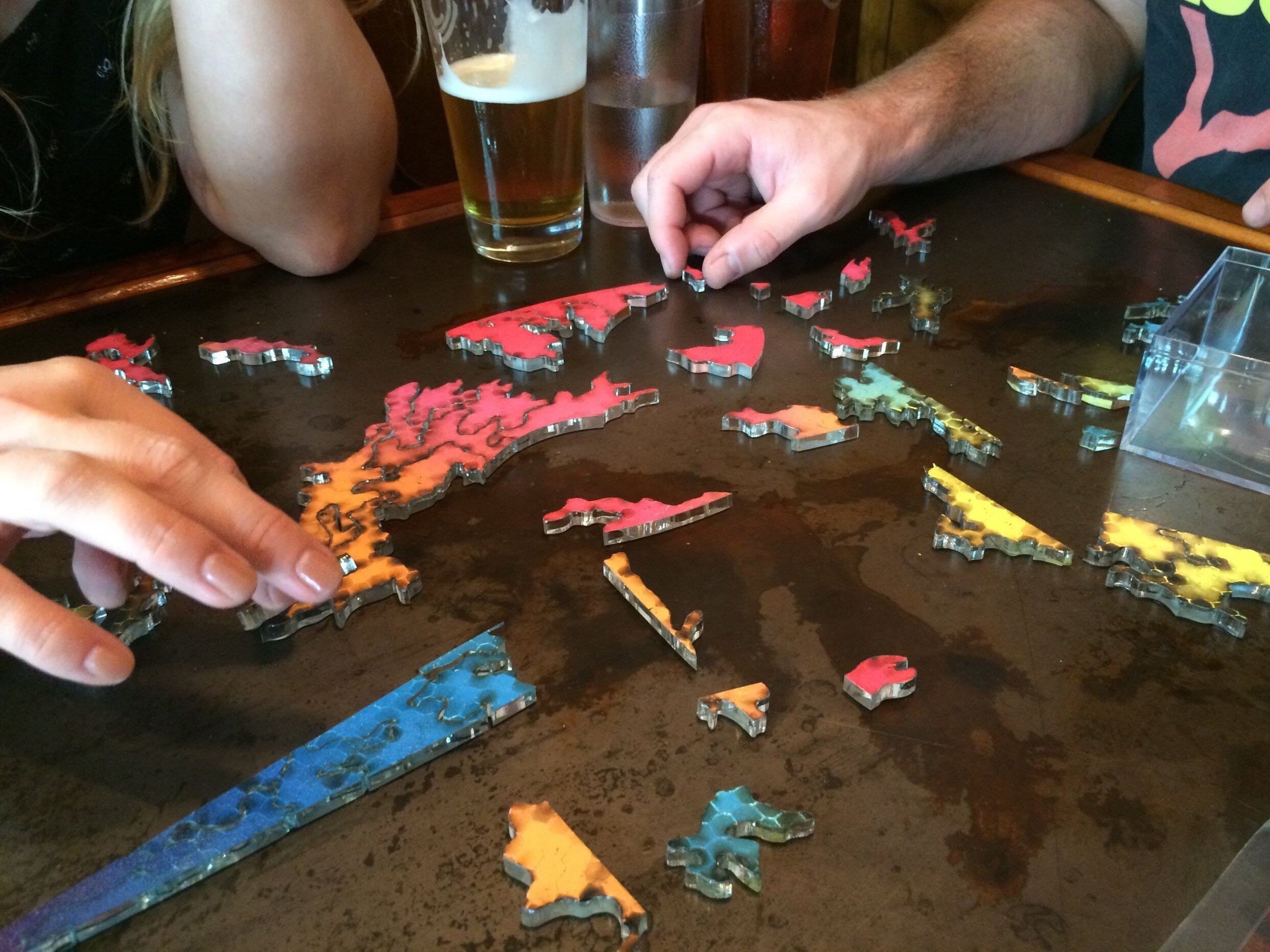 People playing with red orange yellow and blue nike swoosh acrylic puzzle on black table