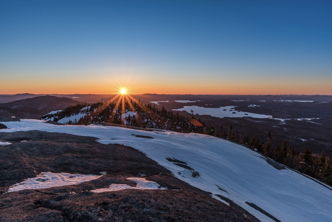 Sunset over the snow-covered Adirondack Mountains, with forest and lakes in the distance.