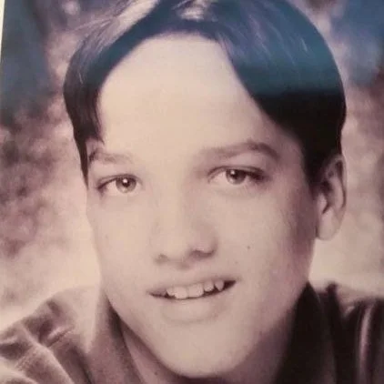 Black and white portrait of a young boy with short dark hair, light eyes, and a slight smile, wearing a collared shirt.