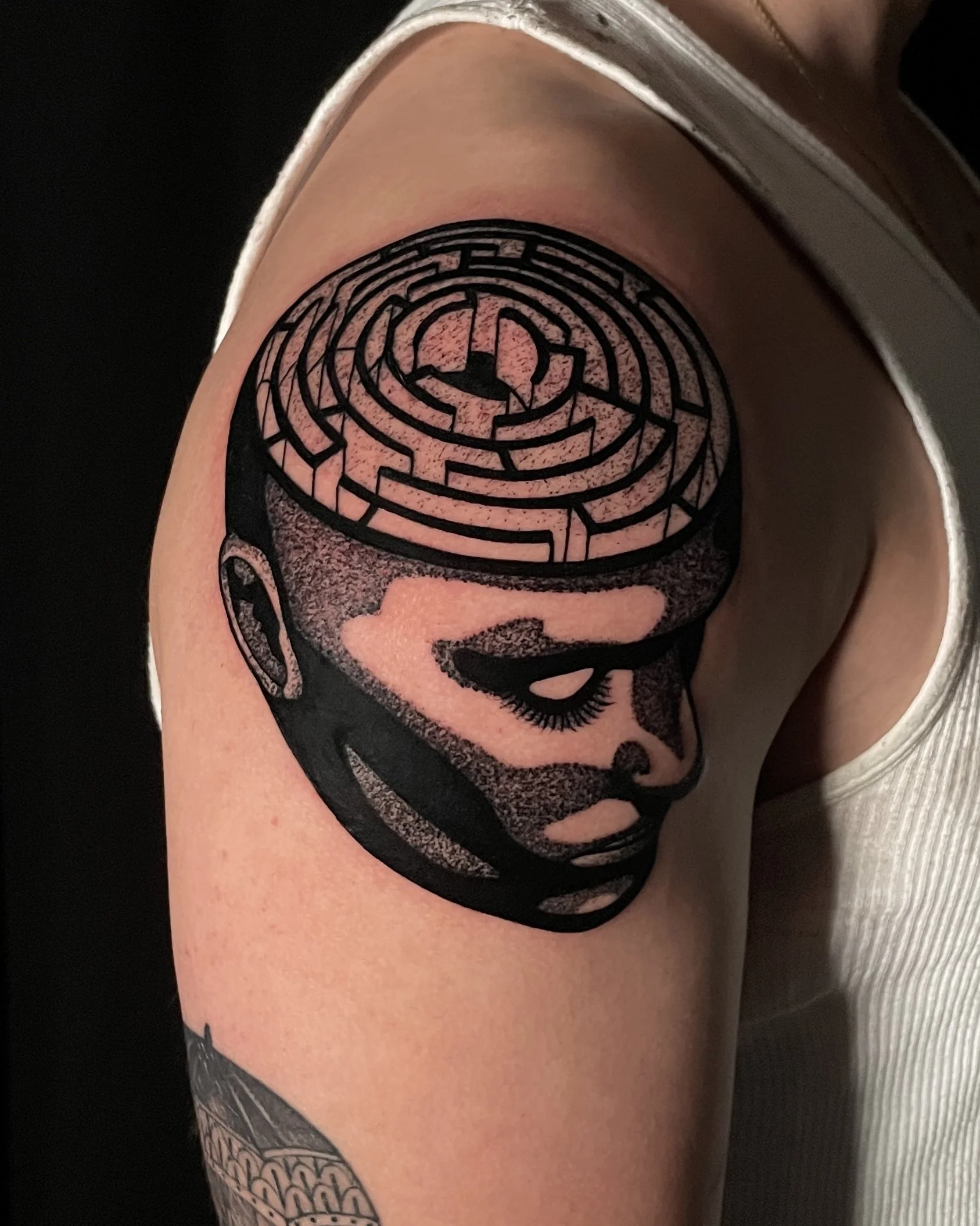 Black and gray tattoo of a woman's face with detailed shading, featuring closed eyes, long eyelashes, earrings, and short hair, and a maze pattern on top of her head.