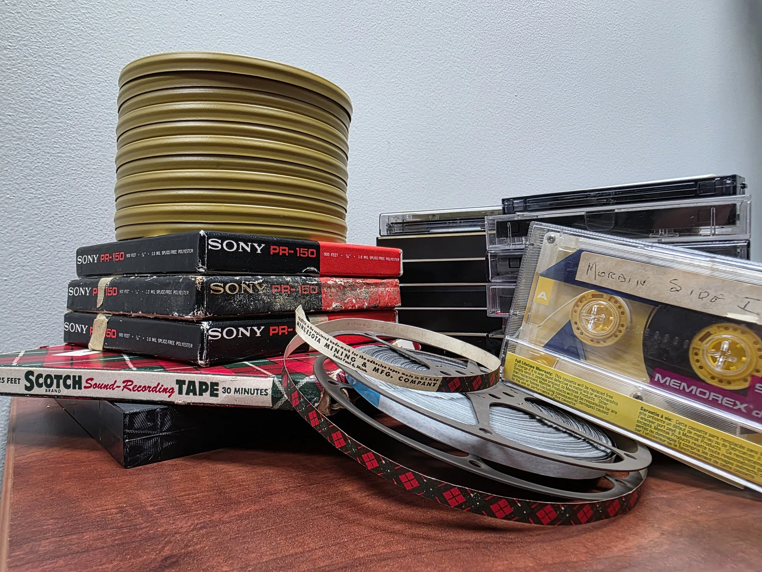 A stack of reel to reel audio in tins, boxes as well as cassette tapes