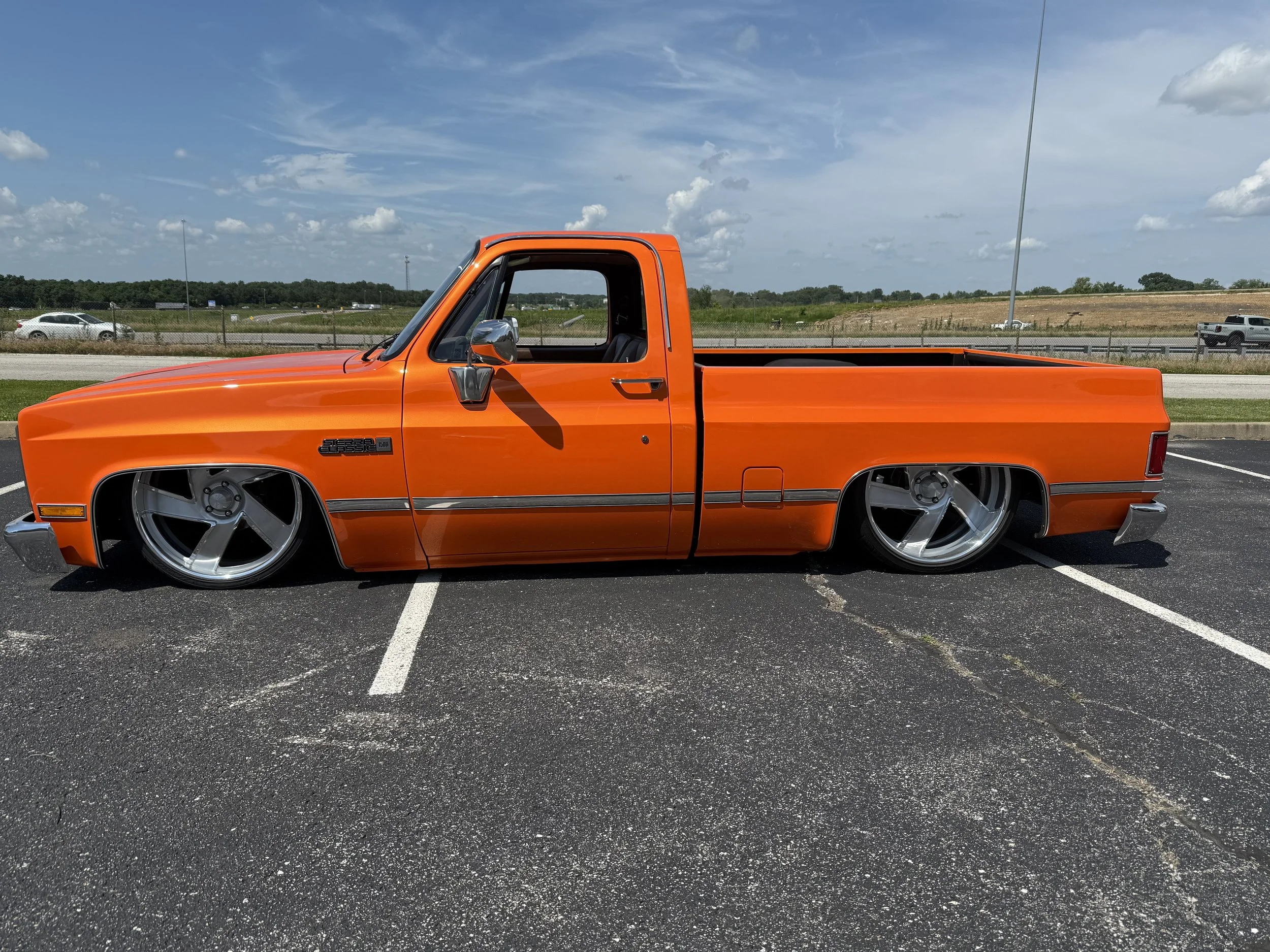Orange lowered pickup truck with large custom silver wheels parked in an empty parking lot.