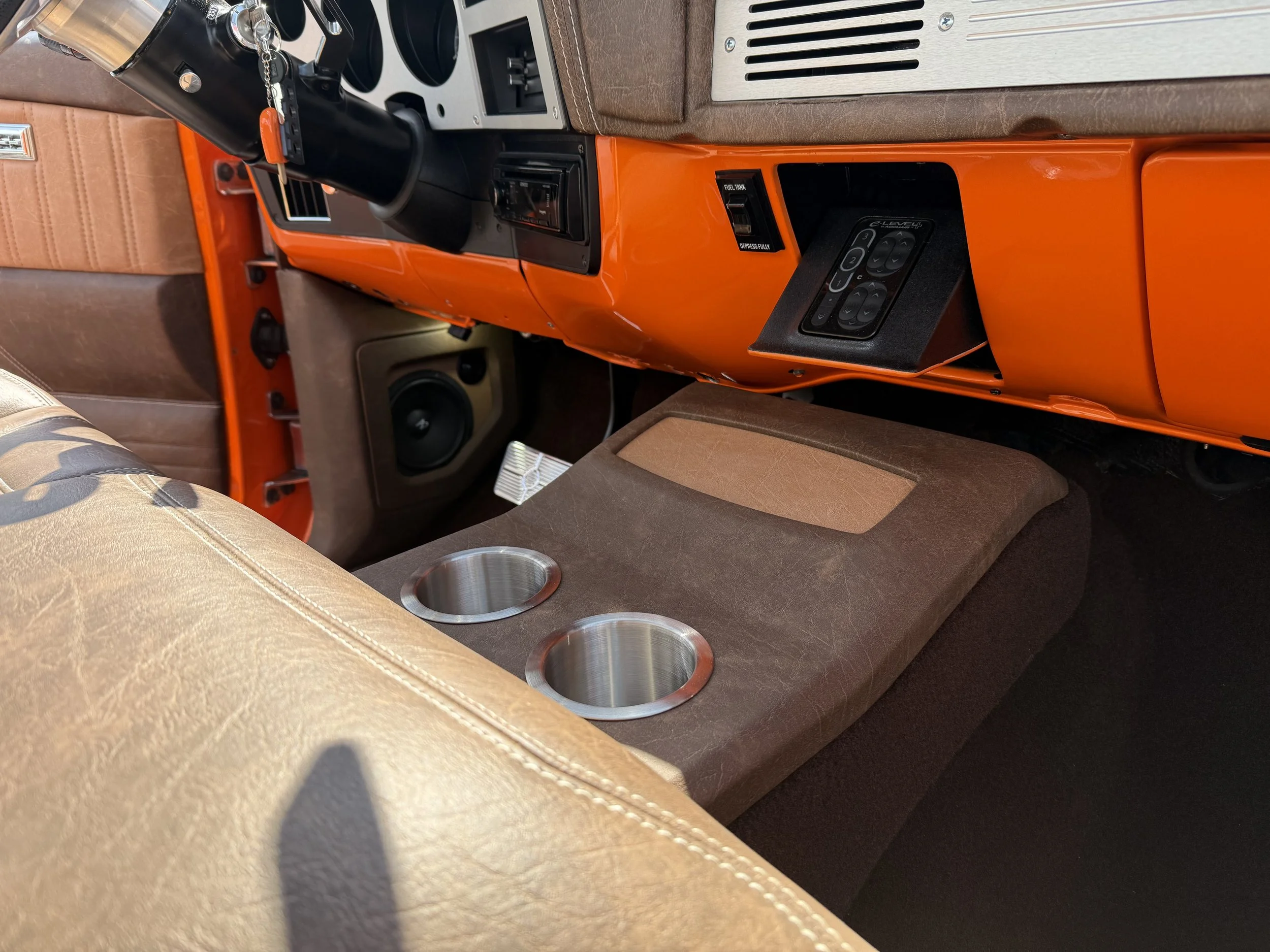 The interior of a vehicle with tan and brown seats, an orange dashboard, a gear shifter, and a speaker on the floor.