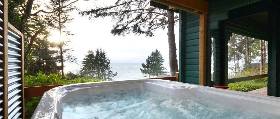 Hot tub on a porch overlooking the ocean with trees and sky in the background.