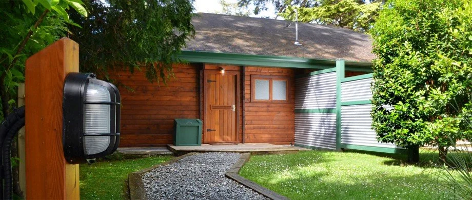 Cabin 9 exterior with gravel pathway with one step leading to front door, surrounded by greenery and trees.