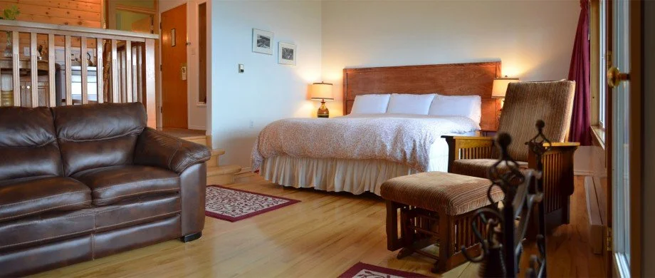 Hotel room with a brown leather sofa, a wooden bed with white bedding, two lamps, a wooden chair, and a sliding glass door with pink curtains.