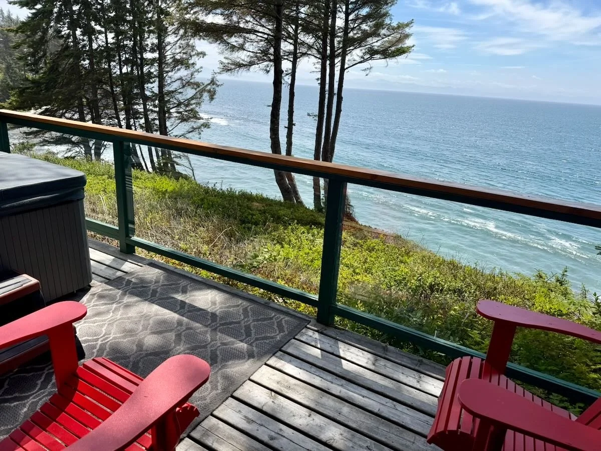 View from deck overlooking the ocean, with hot tub and red adirondack chairs on the deck.