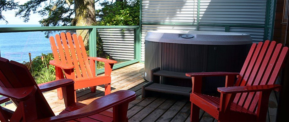 Cabin 9 outdoor deck with four red Adirondack chairs facing each other, a hot tub, and a of the ocean.