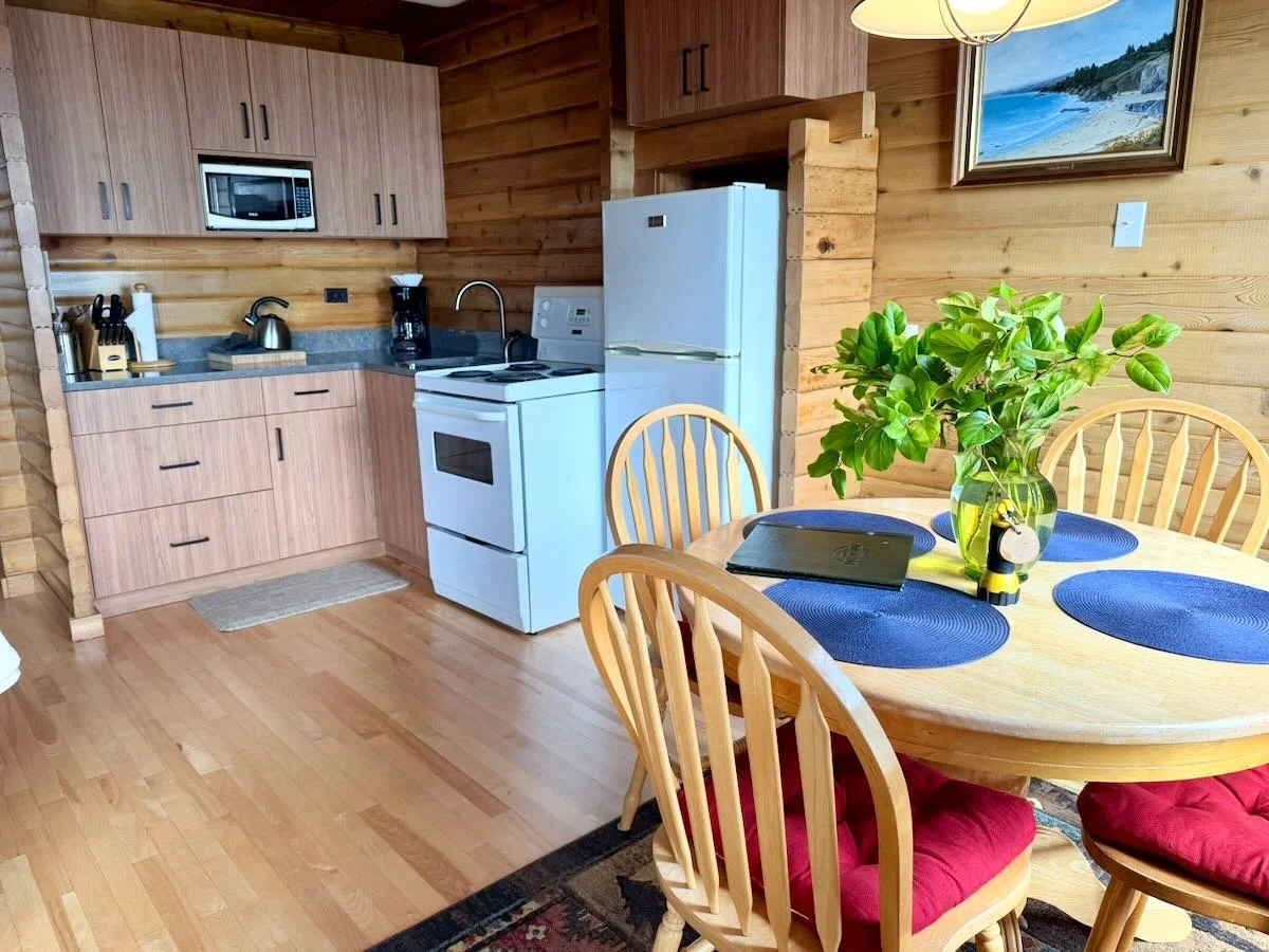 Cabin 10's kitchen and dining area. The kitchen includes light wood cabinets, a microwave, coffee maker, kettle, stove, and a refrigerator.
