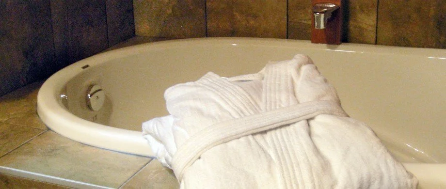 A folded white bathrobe resting on the edge of a bathtub in a bathroom.
