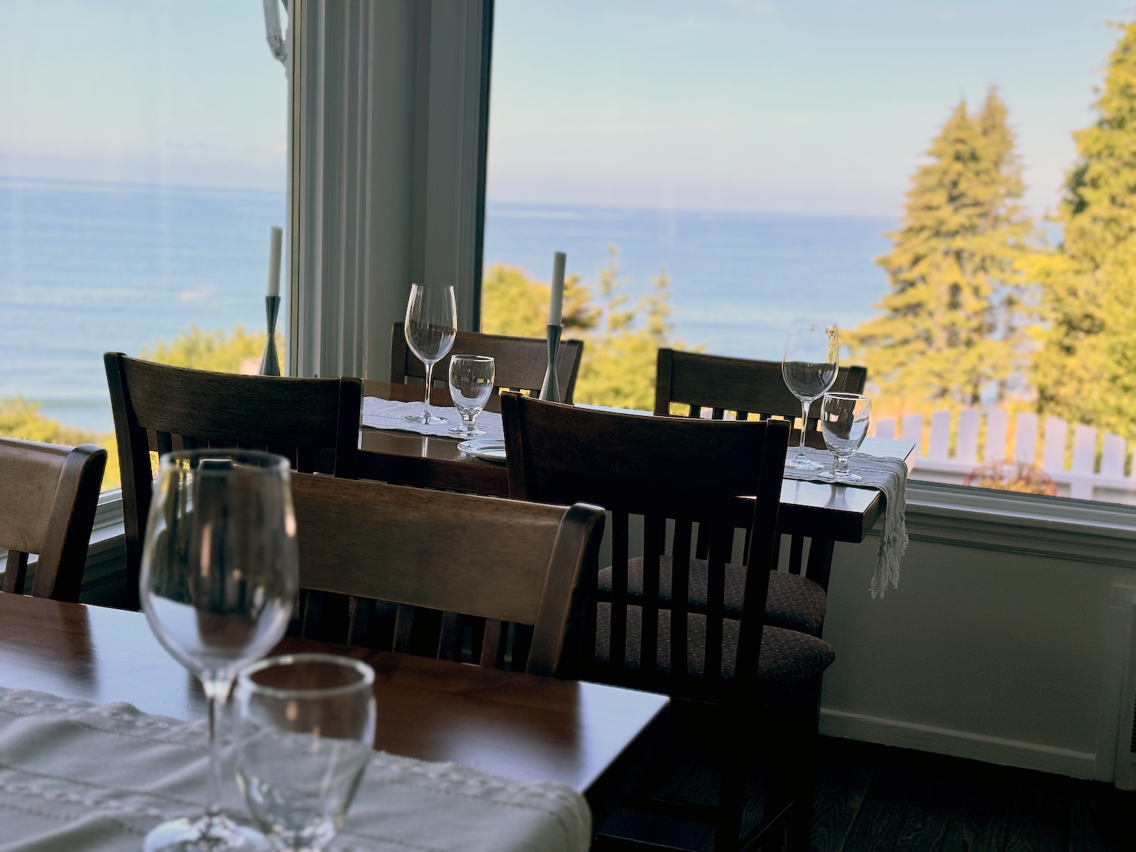 Dining table set with wine glasses and candles near large window overlooking the ocean.