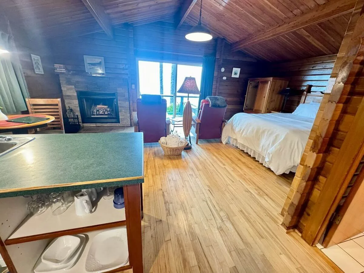 Cabin B interior with a bed, armchairs, a fireplace, and a balcony with a view.