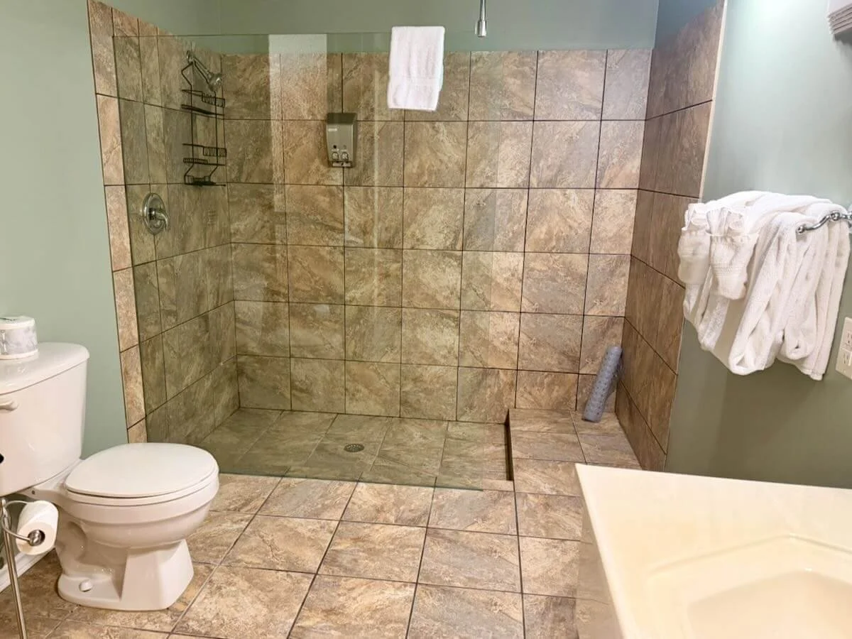 Bathroom with a toilet, a walk-in shower with tiled walls, a towel rack with towels, and a countertop.