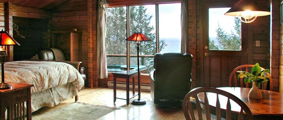Cozy cabin bedroom with a bed, side tables, lamps, and a large window showing trees outside.