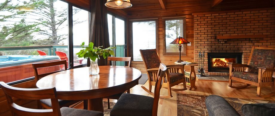 Living room with a wooden dining table, chairs, a hot tub outside, large windows, a fireplace, and cozy seating area.