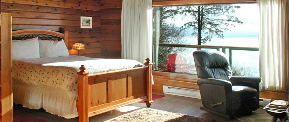 A cozy bedroom with a wooden bed, a leather recliner chair, and a large window overlooking a lake and trees.