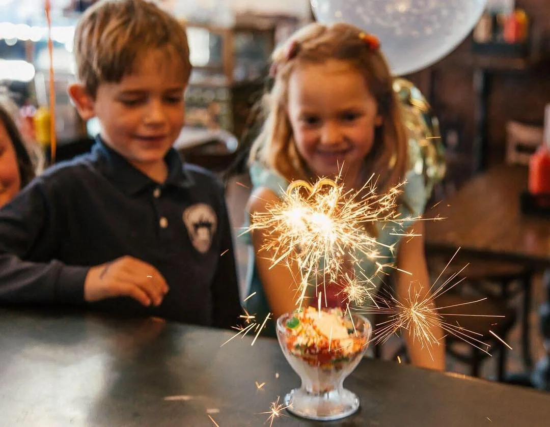 Children celebrating with a dessert topped with sparklers at a party.
