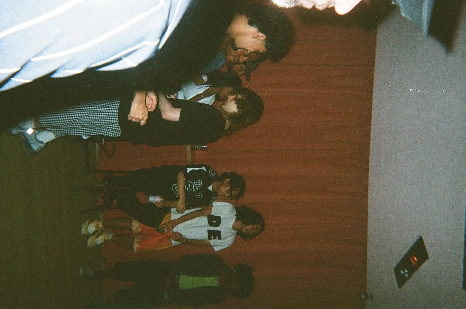 A group of children and adults standing in a line at an indoor event with a red curtain background.