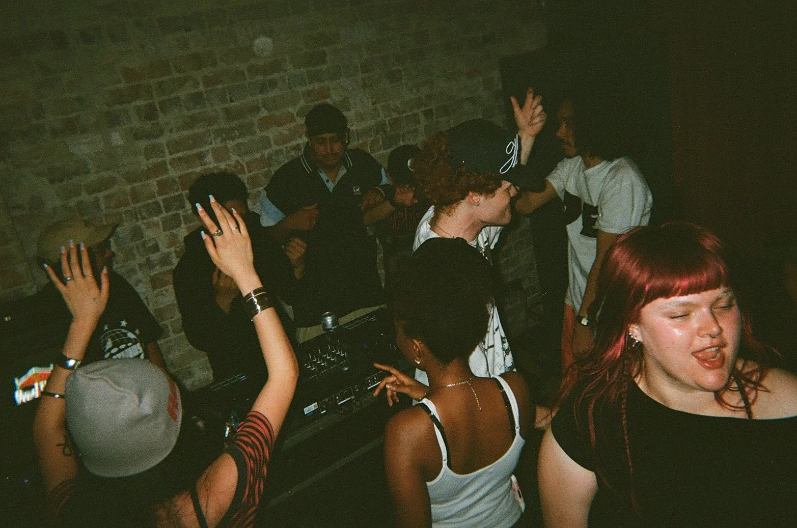 People dancing and enjoying music at a party or club with a brick wall in the background.