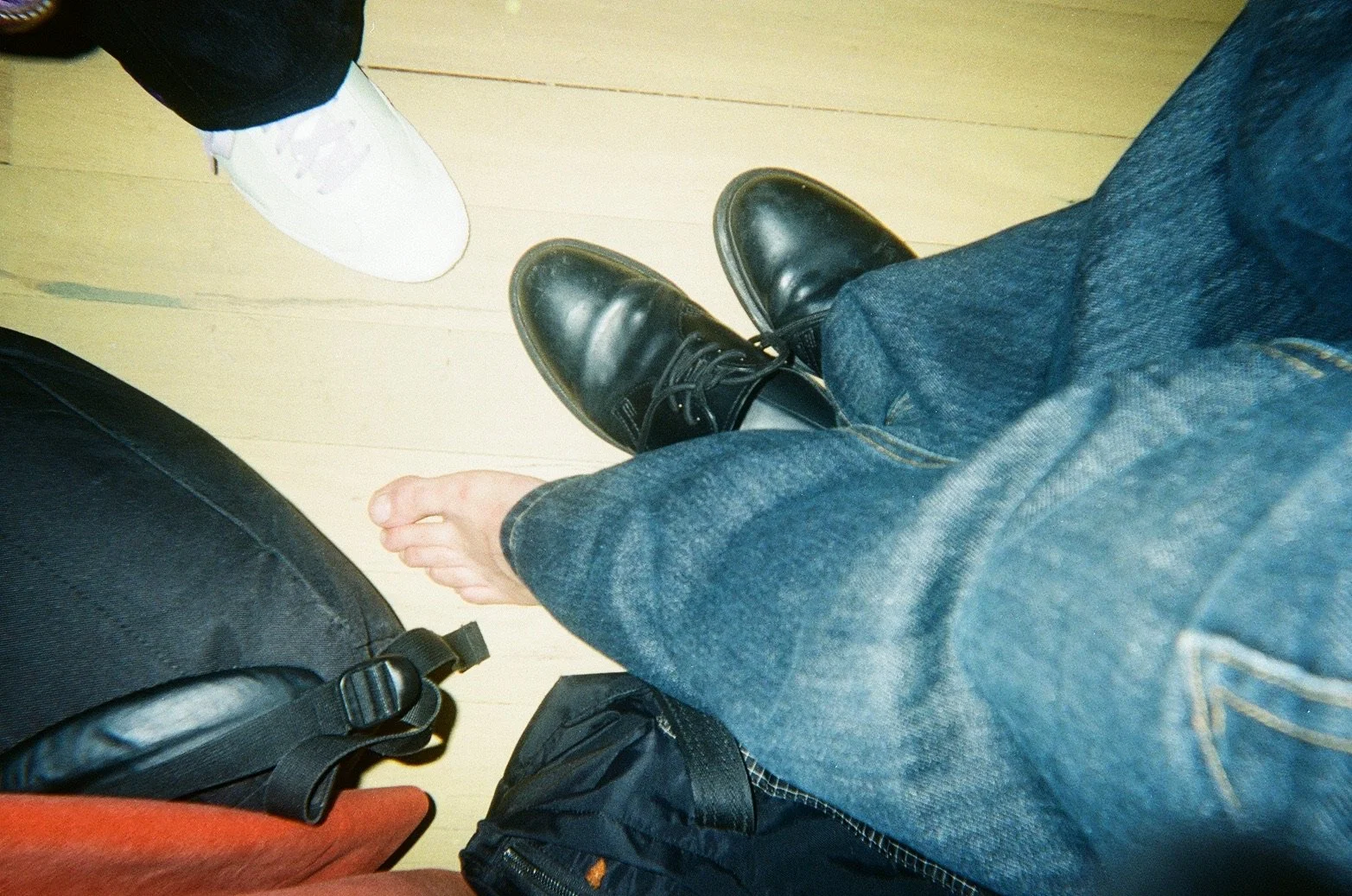 View of a person's legs and feet, showing one foot in black dress shoes and the other in white sneakers, while sitting in a chair on a wooden floor.