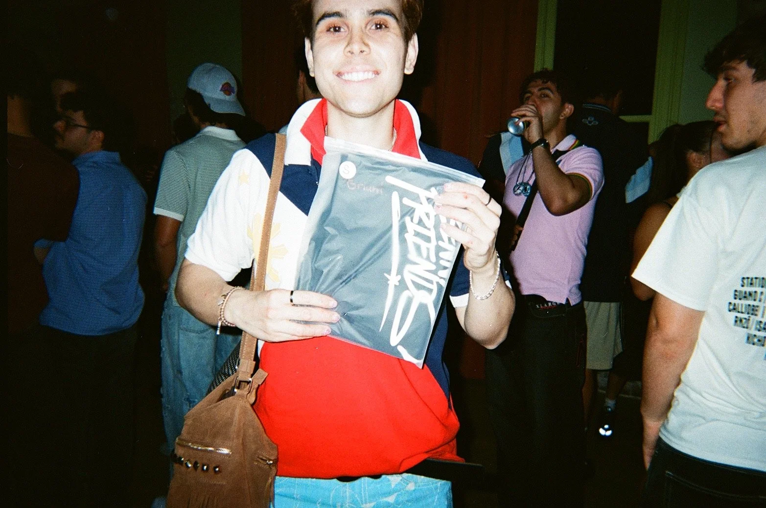 A smiling young man holding a star wars poster at a crowded indoor event.