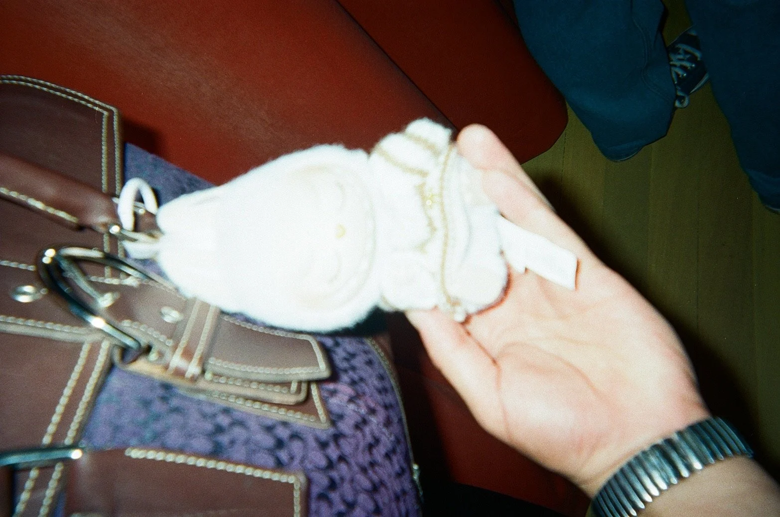 Person holding a white object near a brown bag with gold accents, with a red surface and a person's leg in the background.