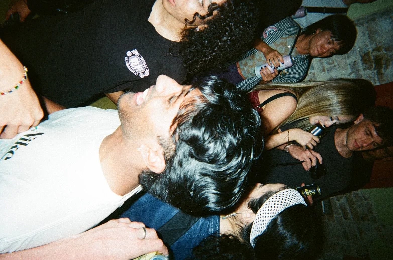Group of people socializing at a party, holding drinks, and standing in a room with brick walls.