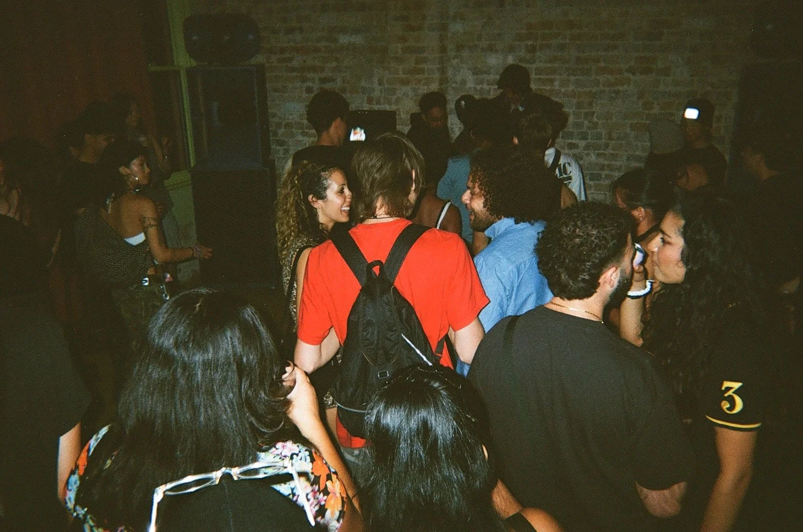 People dancing and socializing in a dimly lit nightclub with brick walls.