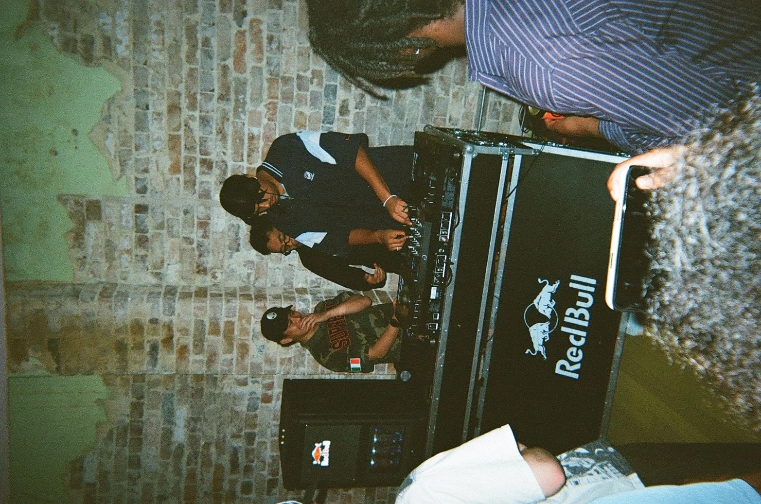 People DJing at a party with a brick wall background and Red Bull music branding.