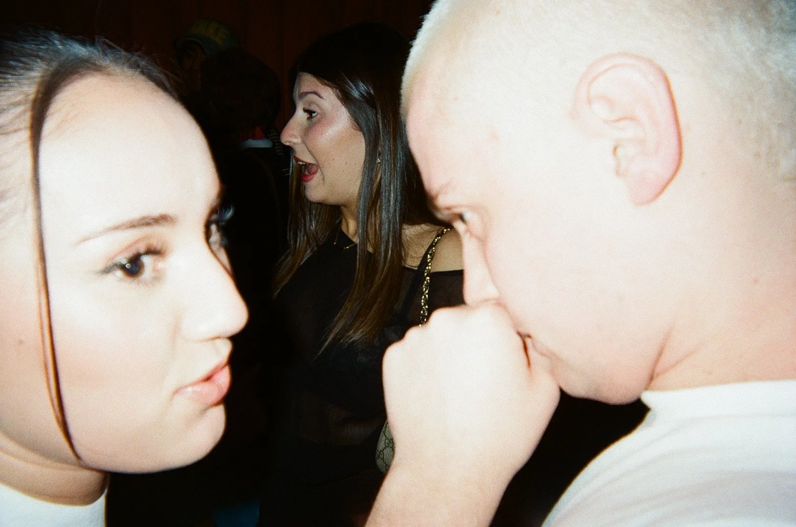Close-up of two women and one man in conversation, with other people in the background at a social event.