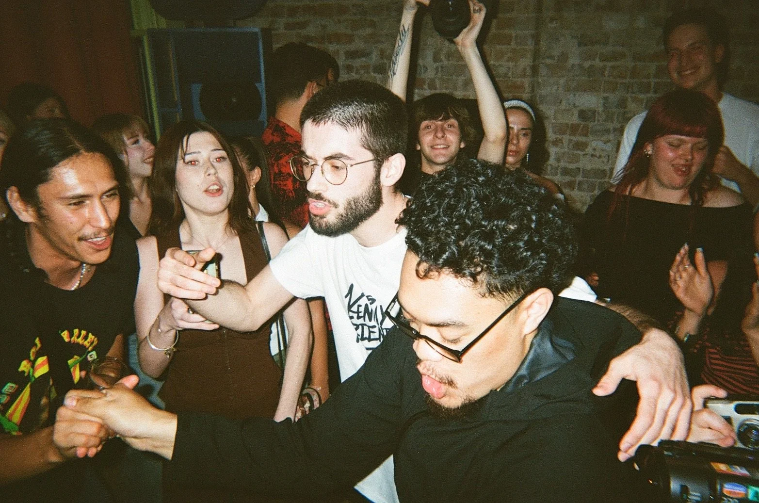 People dancing and socializing at a party with brick walls in the background.