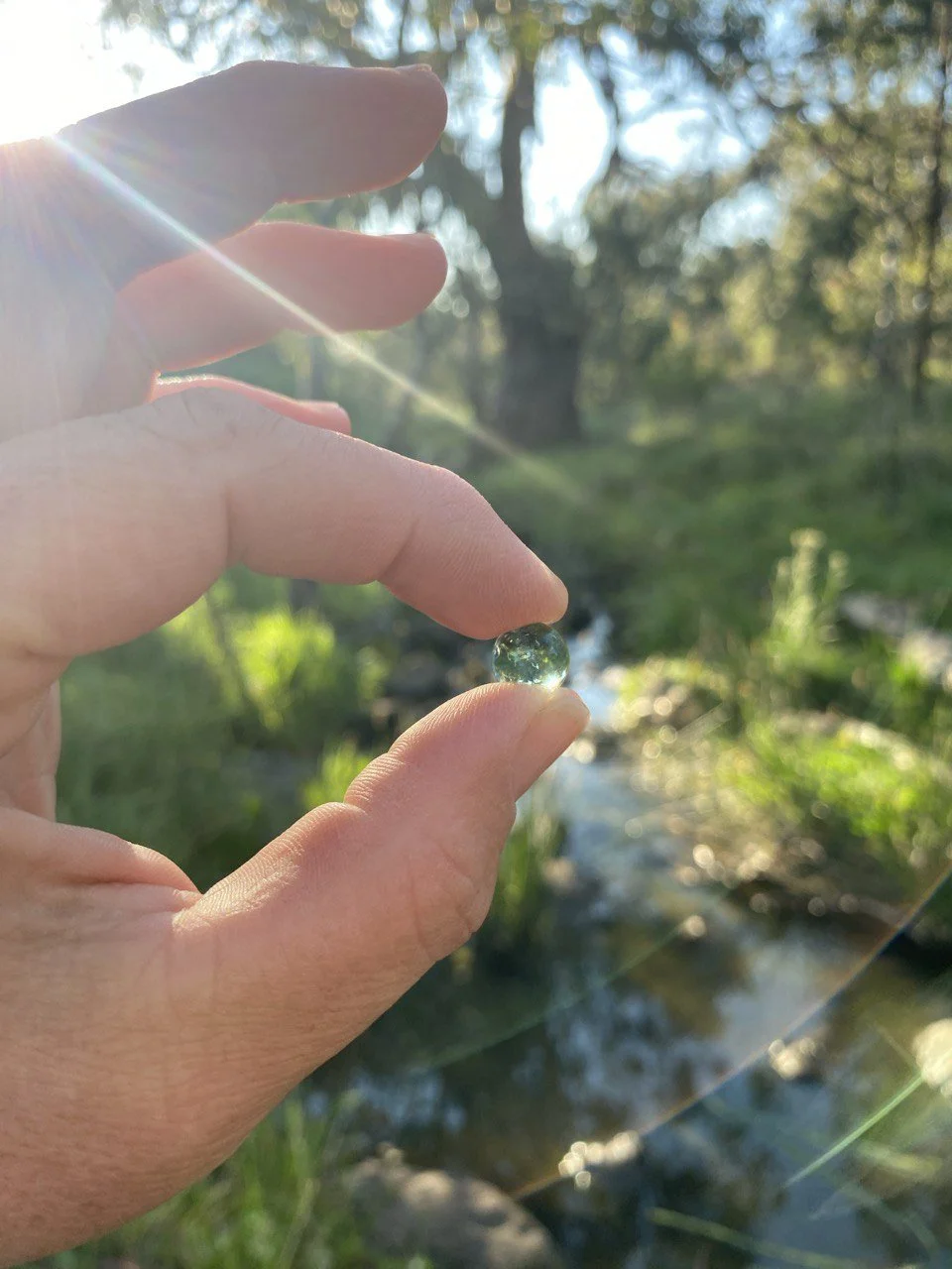 A clear glass marble sitting on a smooth, reflective surface with a bright light source behind it, creating a shadow and reflection.