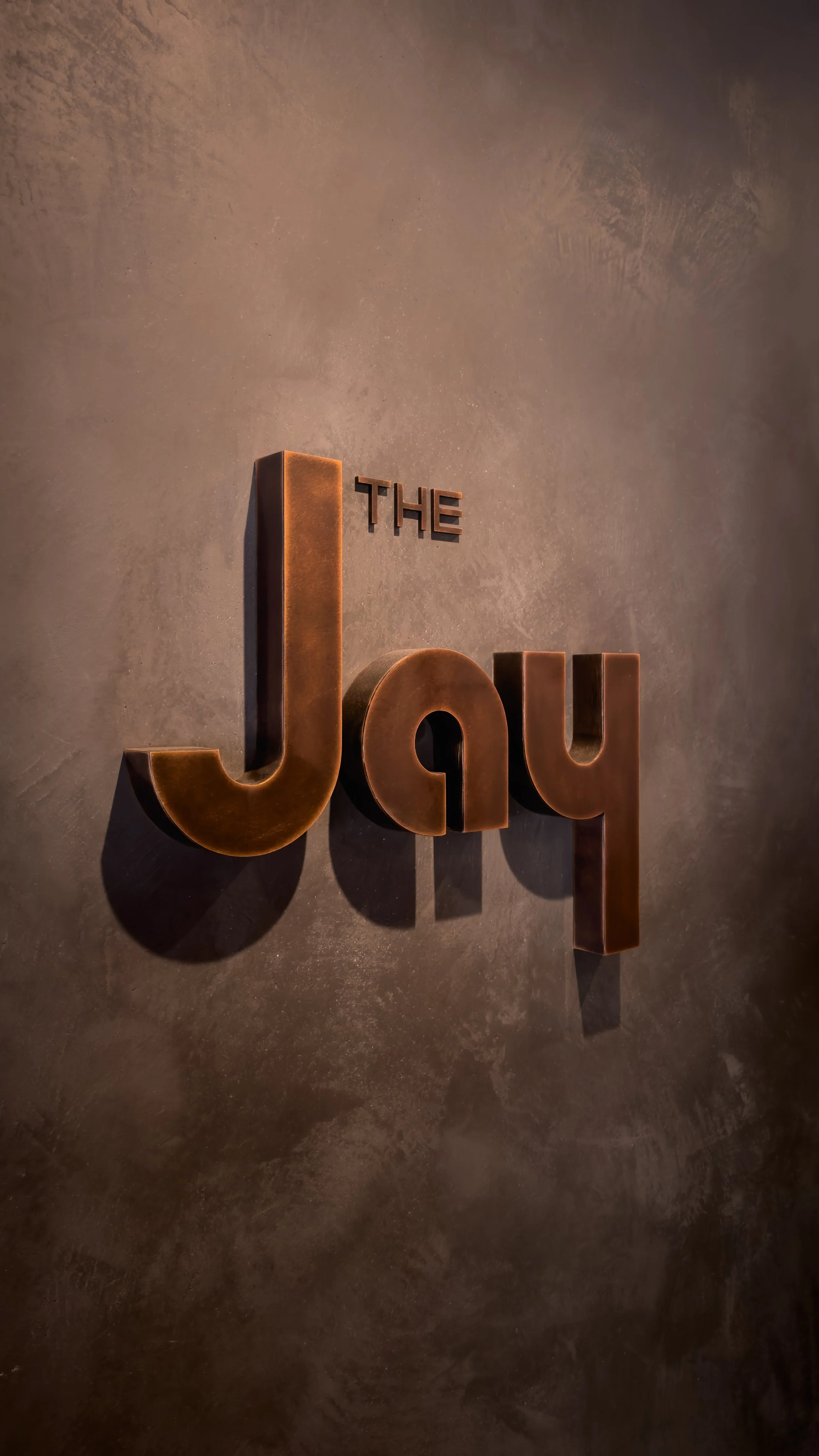 Decorative 3D sign on a textured wall that reads 'The Joy' in large metallic letters.