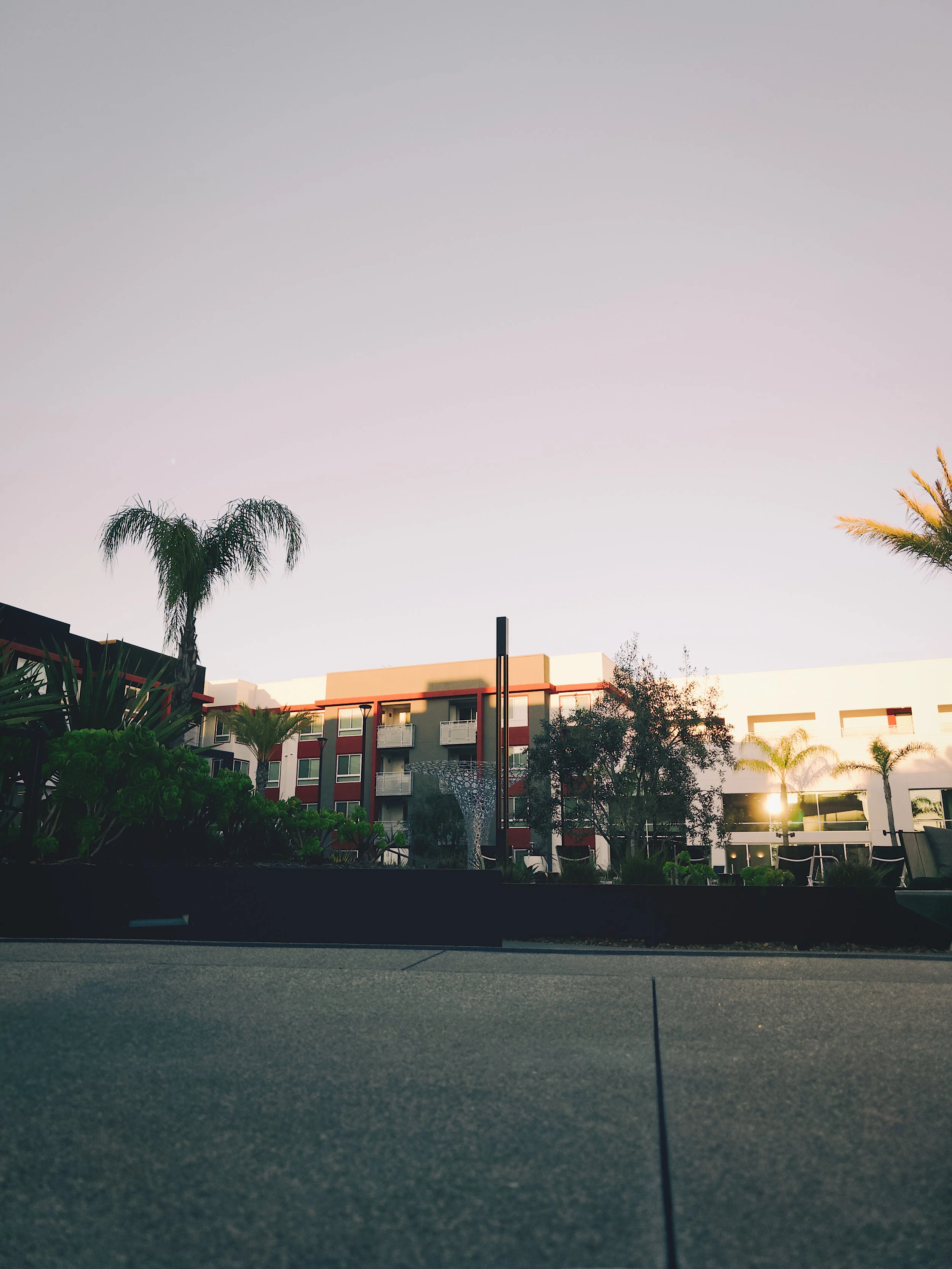 Sunset over a modern apartment complex with palm trees and landscaped greenery.