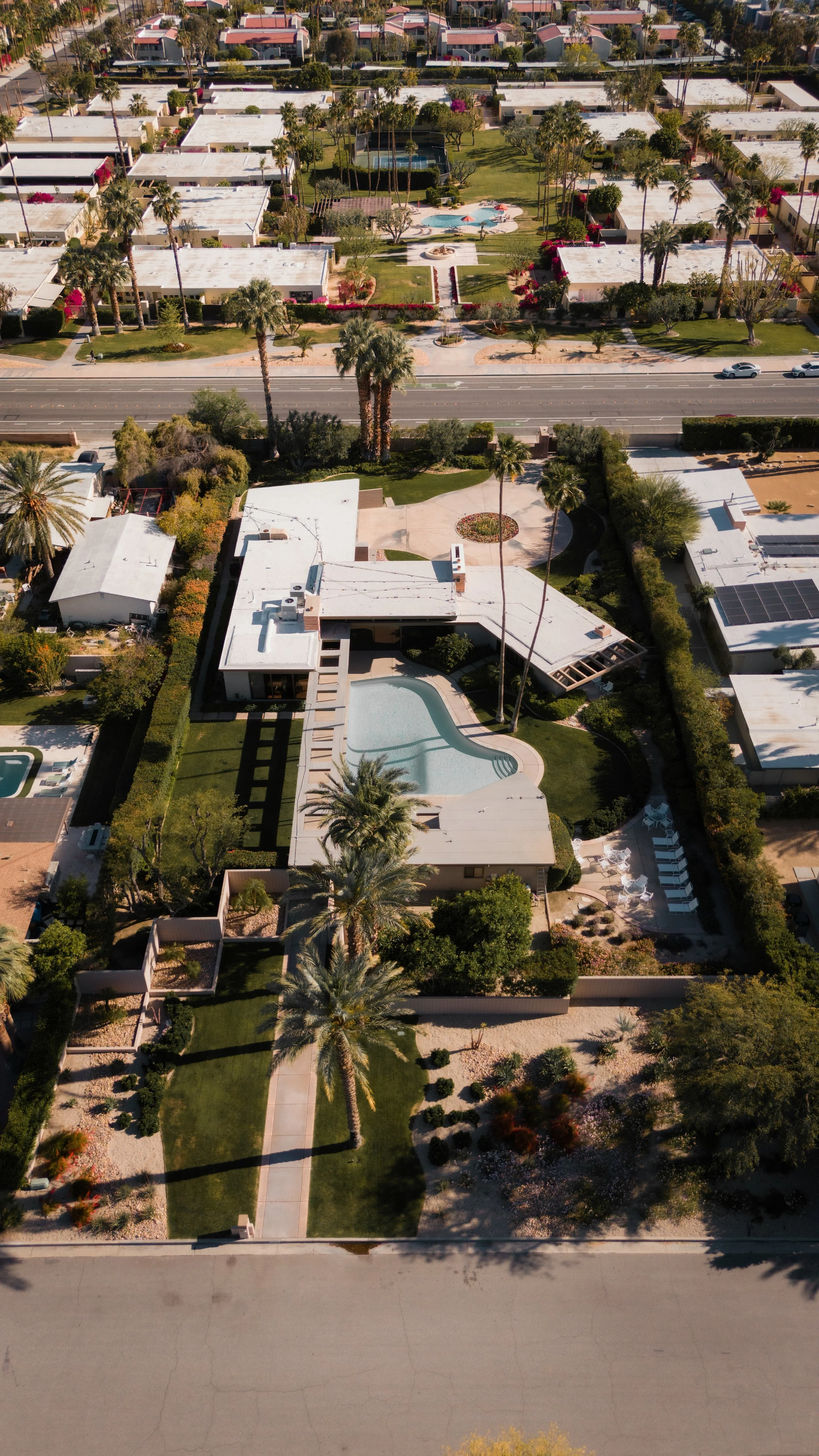 Aerial view of a residential neighborhood with houses, a swimming pool, trees, and a street.