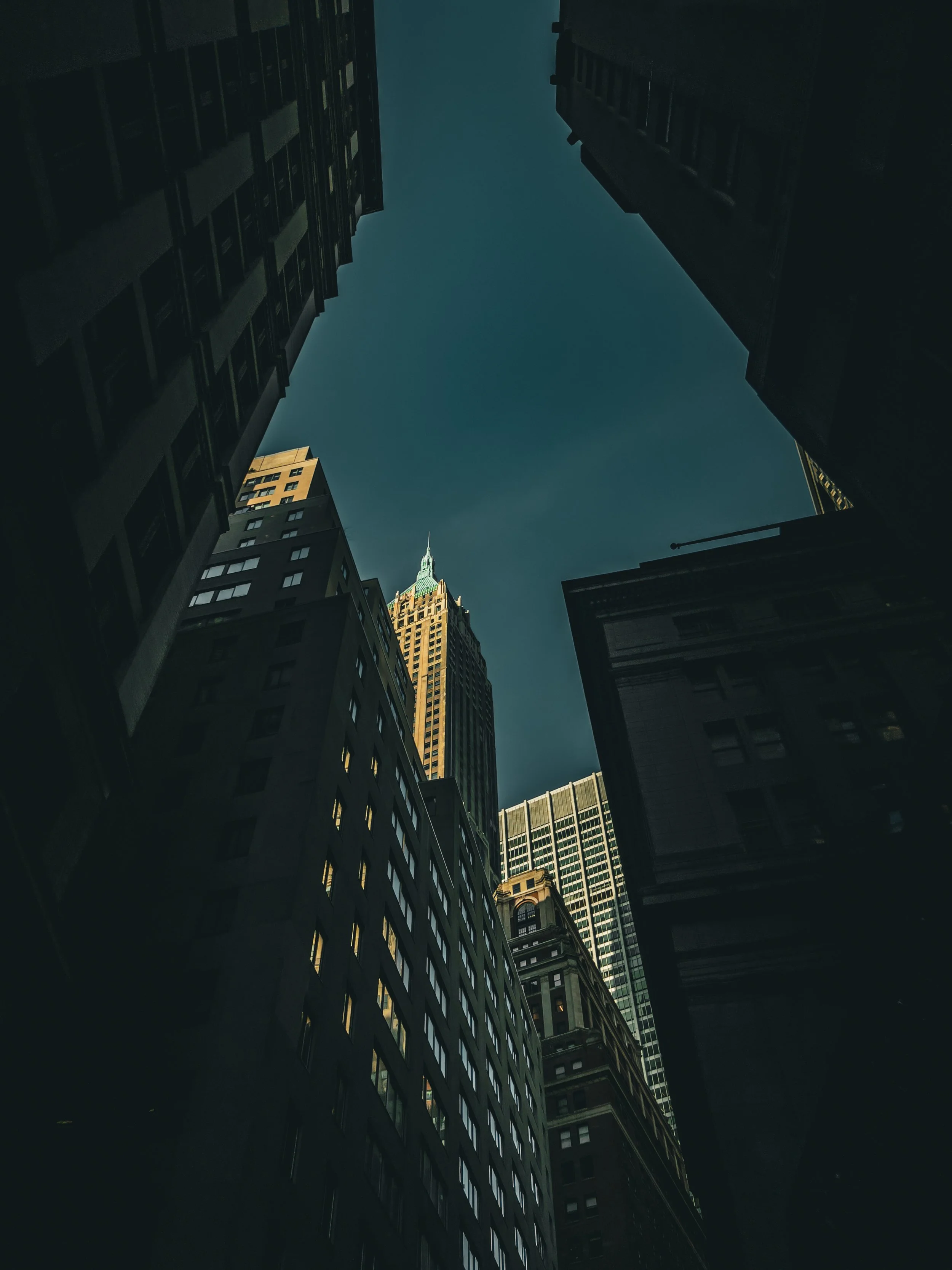 Looking up at tall skyscrapers in a city against a clear blue sky.