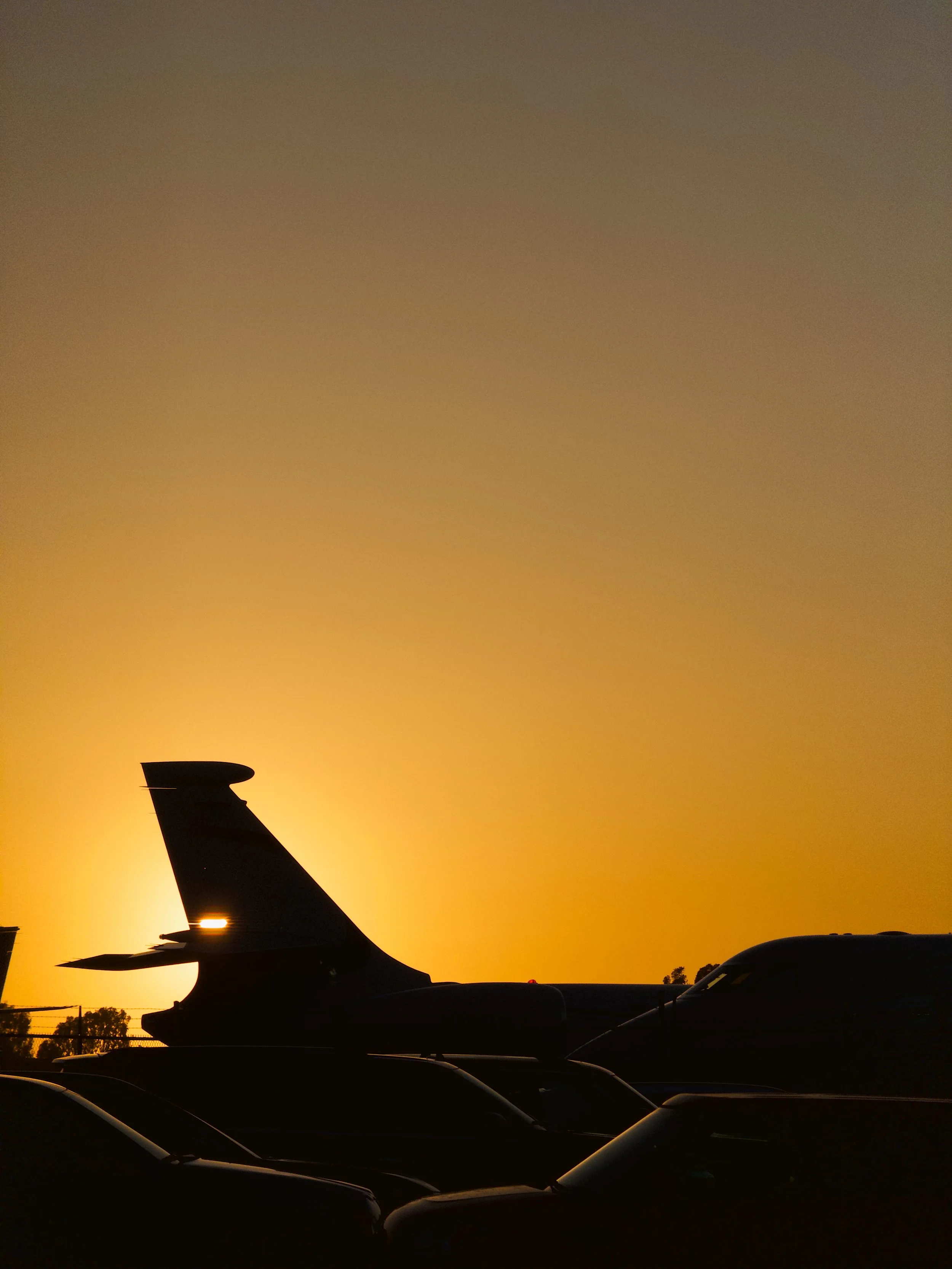 Silhouette of airplanes parked on a tarmac during sunset with a vibrant orange sky.