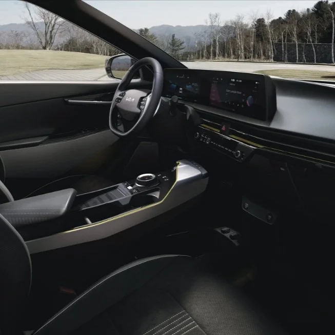 Interno di un'auto moderna con volante, schermo digitale e pannello di controllo centrale, in viaggio su una strada panoramica.