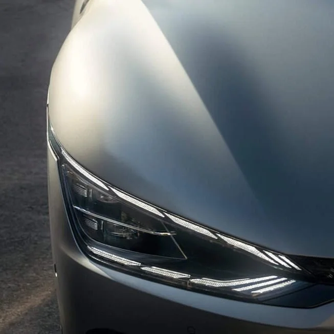 Dettaglio del muso di un'auto moderna grigia, con evidenza sulla linea del cofano e fari di postura avanzata.